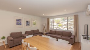 A modern living room with a wooden dining table, brown sofas, and framed pictures on the wall. - Oberlaken - 2/125 Gippsland Street (Jindabyne)
