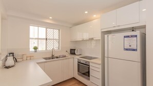 A modern kitchen with white cabinetry, a built-in microwave, a stainless steel sink, and a refrigerator with a freezer. - Oberlaken - 2/125 Gippsland Street (Jindabyne)