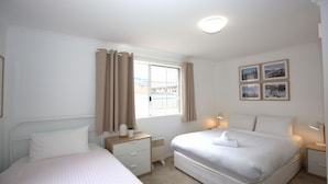 A hotel room with two beds, a window with curtains, a radiator, bedside lamps, and framed pictures on the wall. - Oberlaken - 2/125 Gippsland Street (Jindabyne)