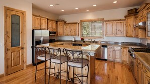 A kitchen with wooden cabinets, a stainless steel refrigerator, a granite countertop, and a window with blinds. - Rock Canyon Ranch Lodge 2 Zion National Park (Orderville)