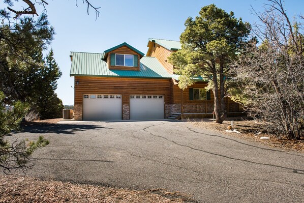 A two-story log cabin with a green metal roof, two garage doors, and a small front porch. - Rock Canyon Ranch Lodge 2 Zion National Park (Orderville)