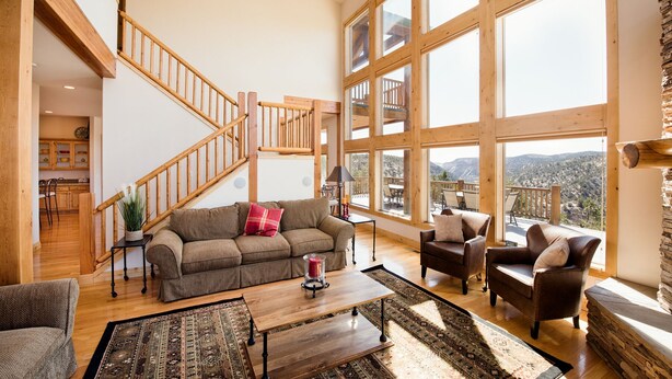 A spacious living room with a wooden staircase, large windows offering a mountain view, and a cozy seating area. - Rock Canyon Ranch Lodge 2 Zion National Park (Orderville)
