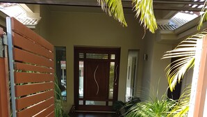 Una escalera de madera que conduce a una puerta con diseño decorativo, rodeada de follaje y rocas.