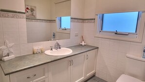 Un baño con lavamanos blanco, espejo y ventana.