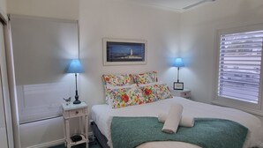 Un dormitorio con cama, dos lámparas de noche, un cuadro enmarcado en la pared y una ventana con persianas.