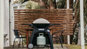 A patio area with a grill, two chairs, and a wooden fence.