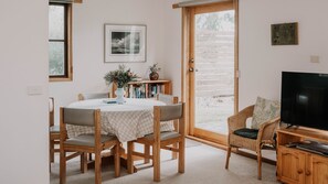 Ein gemütliches Zimmer mit rundem Tisch, Stühlen, einem Bücherregal, einem Fernseher und einer Tür zum Außenbereich.