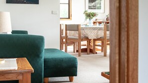 Une pièce avec un fauteuil vert, une table en bois et un coin repas comprenant des chaises et une table dressée pour deux personnes.