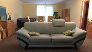 A living room with a grey sofa, a coffee table, and a dining area with a table and chairs. - Appartements Funk (Pfungstadt)