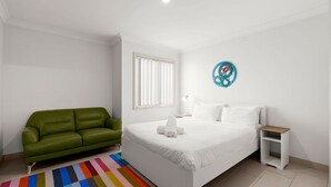 Une chambre avec un canapé vert, un lit blanc, un tapis rayé aux couleurs vives, une table de chevet et un élément décoratif mural.
