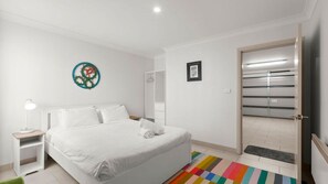 Une chambre à coucher avec un lit, une table de chevet, une armoire, une porte et un tapis rayé aux couleurs vives.