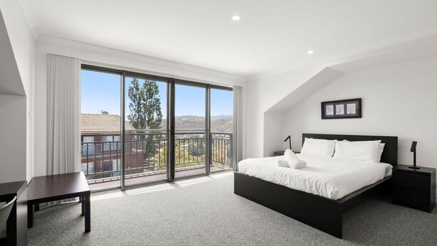 Une chambre dotée d’un grand lit, d’un bureau et d’un balcon offrant une vue sur le paysage.