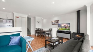 Un salon moderne comprenant un canapé, une table basse, un téléviseur, une cheminée et un coin repas avec des chaises et une table.