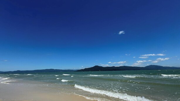 A beach with clear skies and distant mountains. - Encanto na Praia da Daniela \- Florianópolis \- SC (Florianópolis)