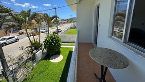A balcony with a small table, a view of the street, and some greenery. - Encanto na Praia da Daniela \- Florianópolis \- SC (Florianópolis)