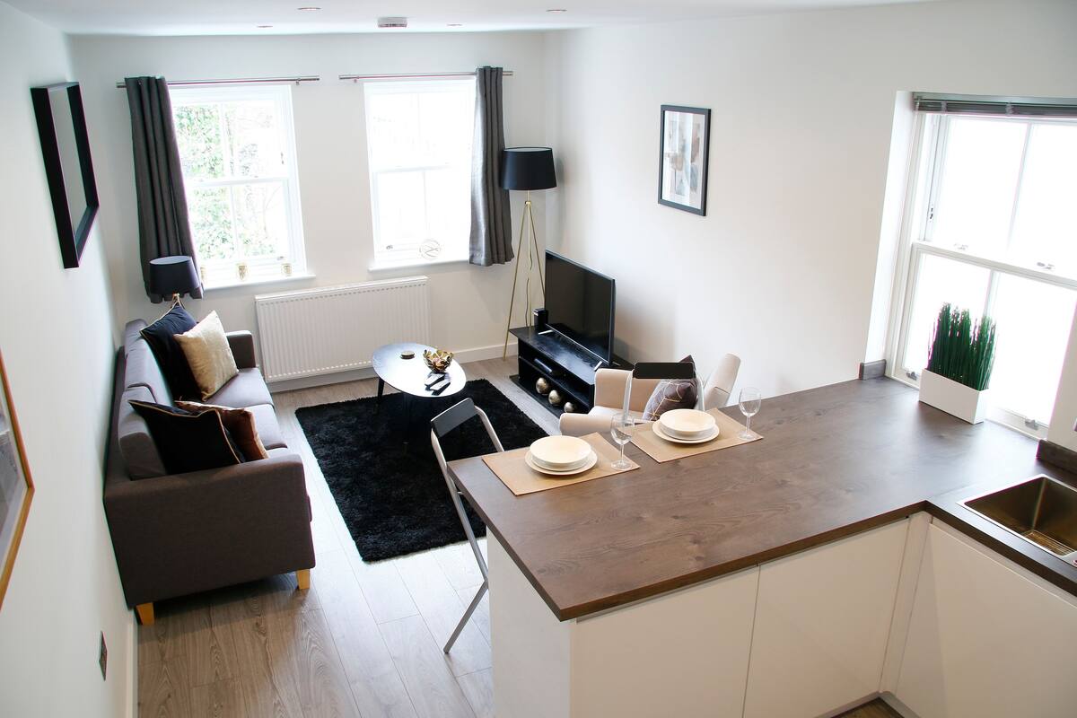 Uma sala de estar moderna com um sofá, uma mesa de jantar e uma cozinha com bancada e pia.