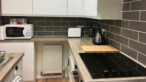 A modern kitchen with white cabinets, a black tiled backsplash, a microwave, a toaster, a kettle, and a stove. - Highfield University House (Southampton)