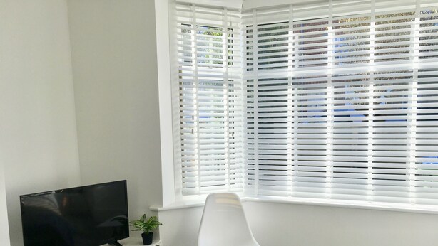 A room with a television on a shelf, a white chair, and a window with blinds. - Highfield University House (Southampton)