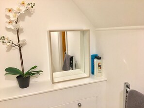 A bathroom with a white vanity, a mirror, a potted orchid, and toiletries on the shelf. - Highfield University House (Southampton)
