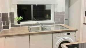 A compact kitchen with a built-in washing machine, a window with a view, and a small potted plant. - Highfield University House (Southampton)