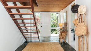 A hallway with a wooden ladder, a white door leading outside, and a wall with hats and a woven bag. - Cape Breeze - 5 BR home with headland views (Byron Bay)