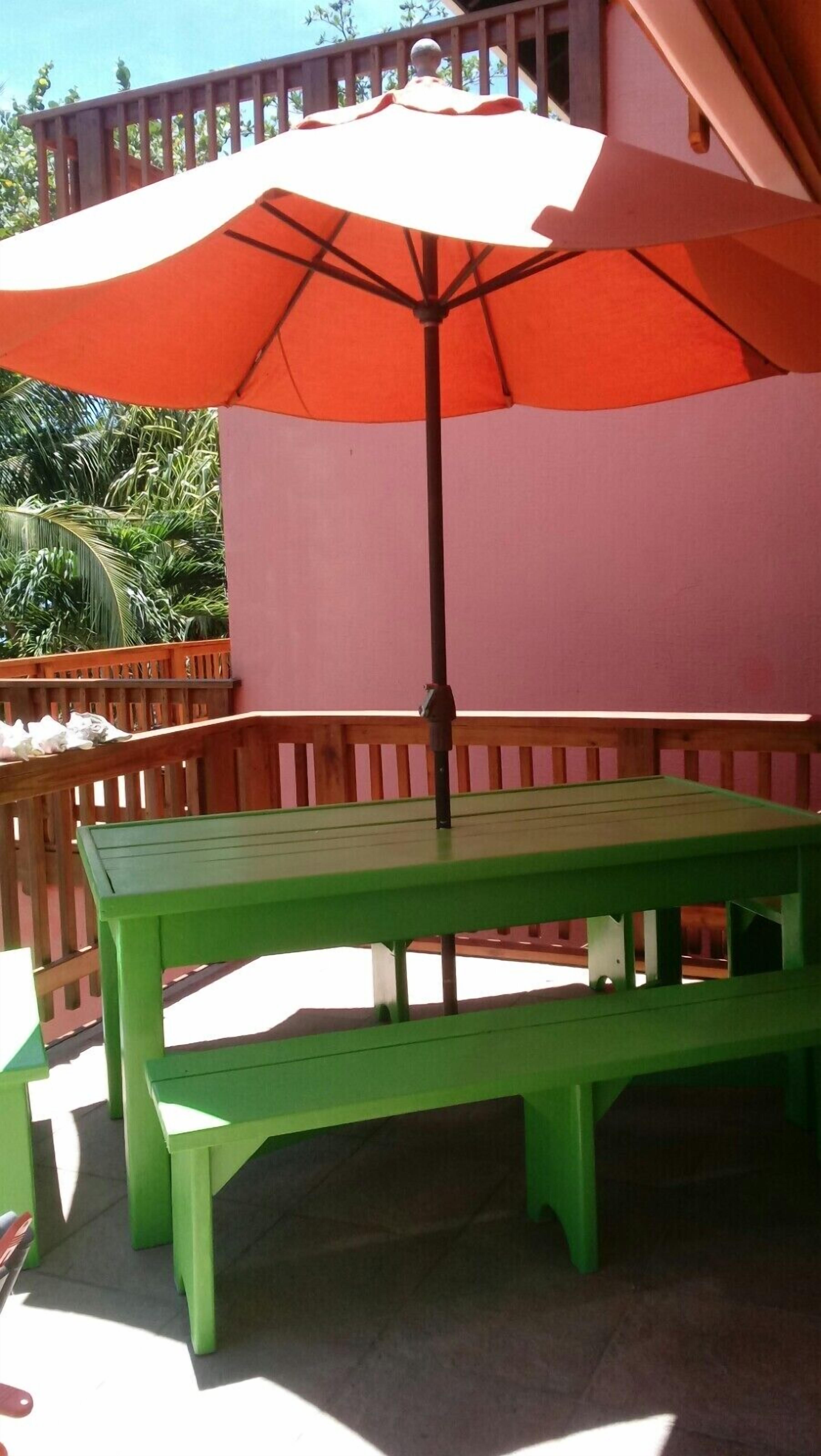 Mesa de picnic verde con banco a juego bajo un paraguas naranja grande.