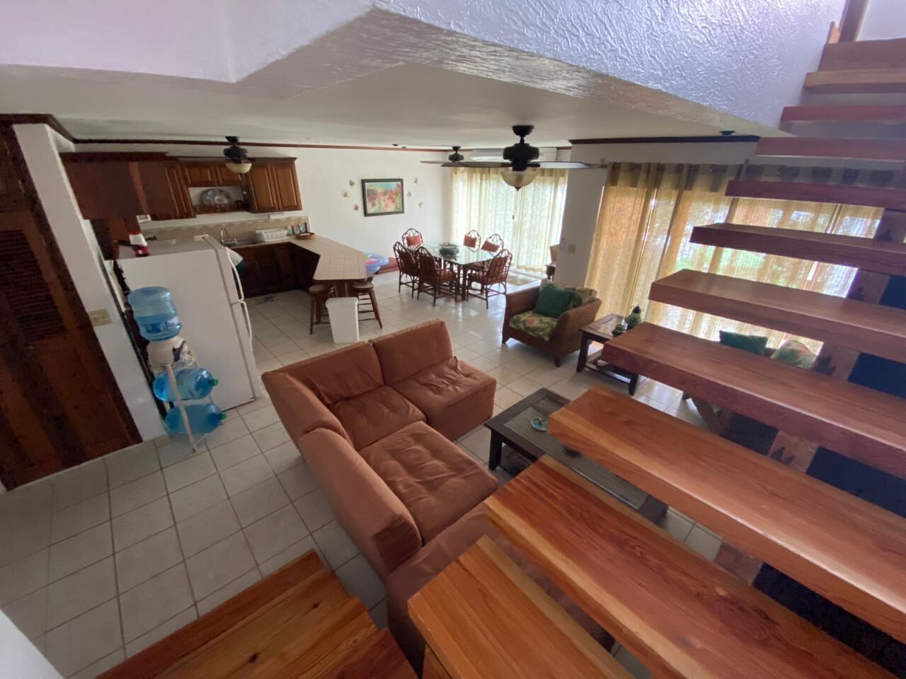 Amplia sala de estar con sofá, bancos de madera, mesa de comedor y cocina al fondo.