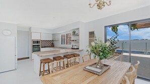 A modern kitchen with white cabinetry, a central island with stools, and a dining area with a wooden table and chairs. - 10 Ocean Drive - one of those properties that  will have you never wanting to leave (Port Fairy)