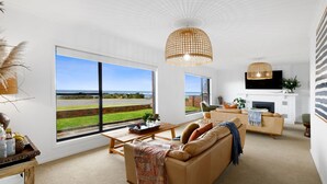 A spacious living room with large windows, a fireplace, and a modern chandelier. - 10 Ocean Drive - one of those properties that  will have you never wanting to leave (Port Fairy)