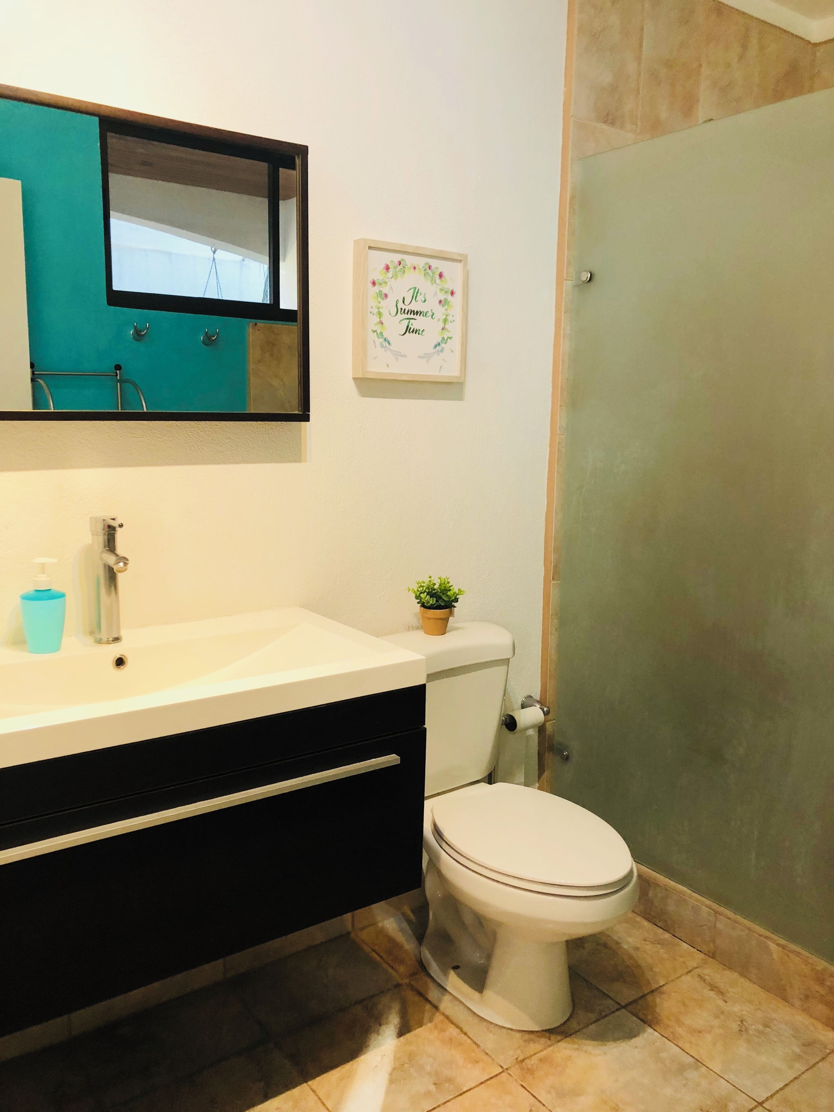 A bathroom with a white sink, a mirror, a toilet, and a shower enclosure.
