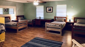 A room with two single beds, a desk, a chair, a ceiling fan, and a window with blinds.