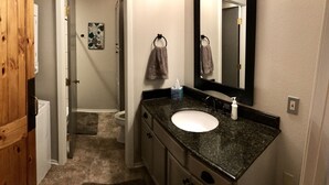 A bathroom with a wooden door, a sink with a black countertop, a mirror, and a towel hanging on a hook.