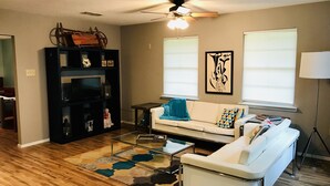 A living room with a sofa, a coffee table, a black entertainment unit, and a ceiling fan.
