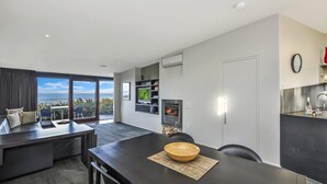 A modern living room with a large window overlooking the ocean, a fireplace, and a dining area with a black table and chairs. - Hearns Beachside Villa 1 (Port Fairy)