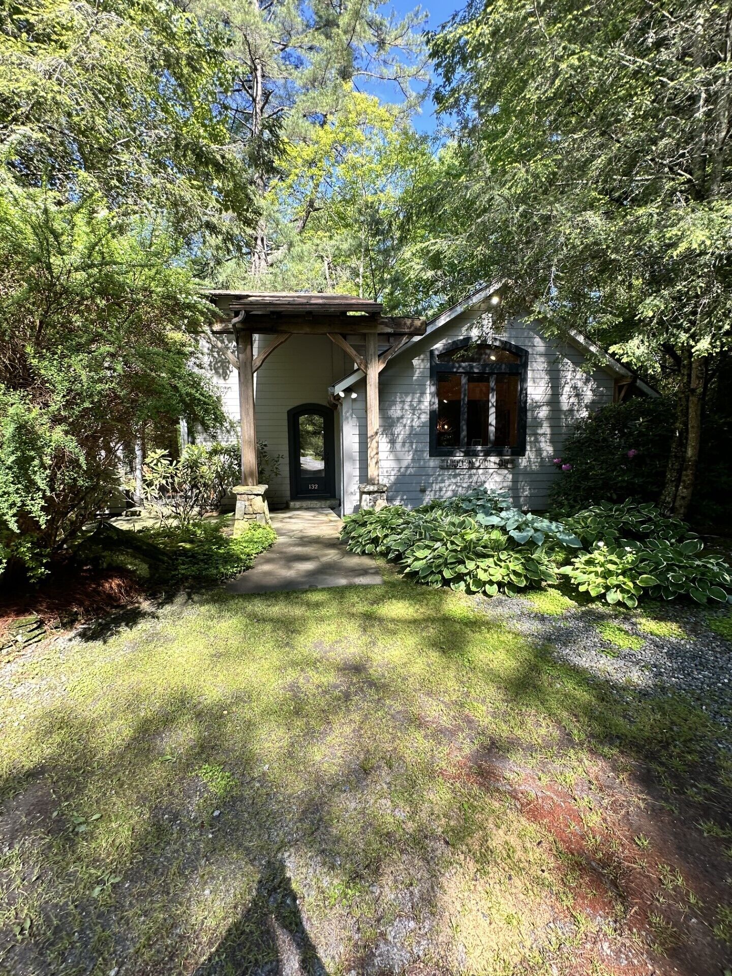 A rustic cabin with a wooden porch, surrounded by lush greenery and a clear sky.