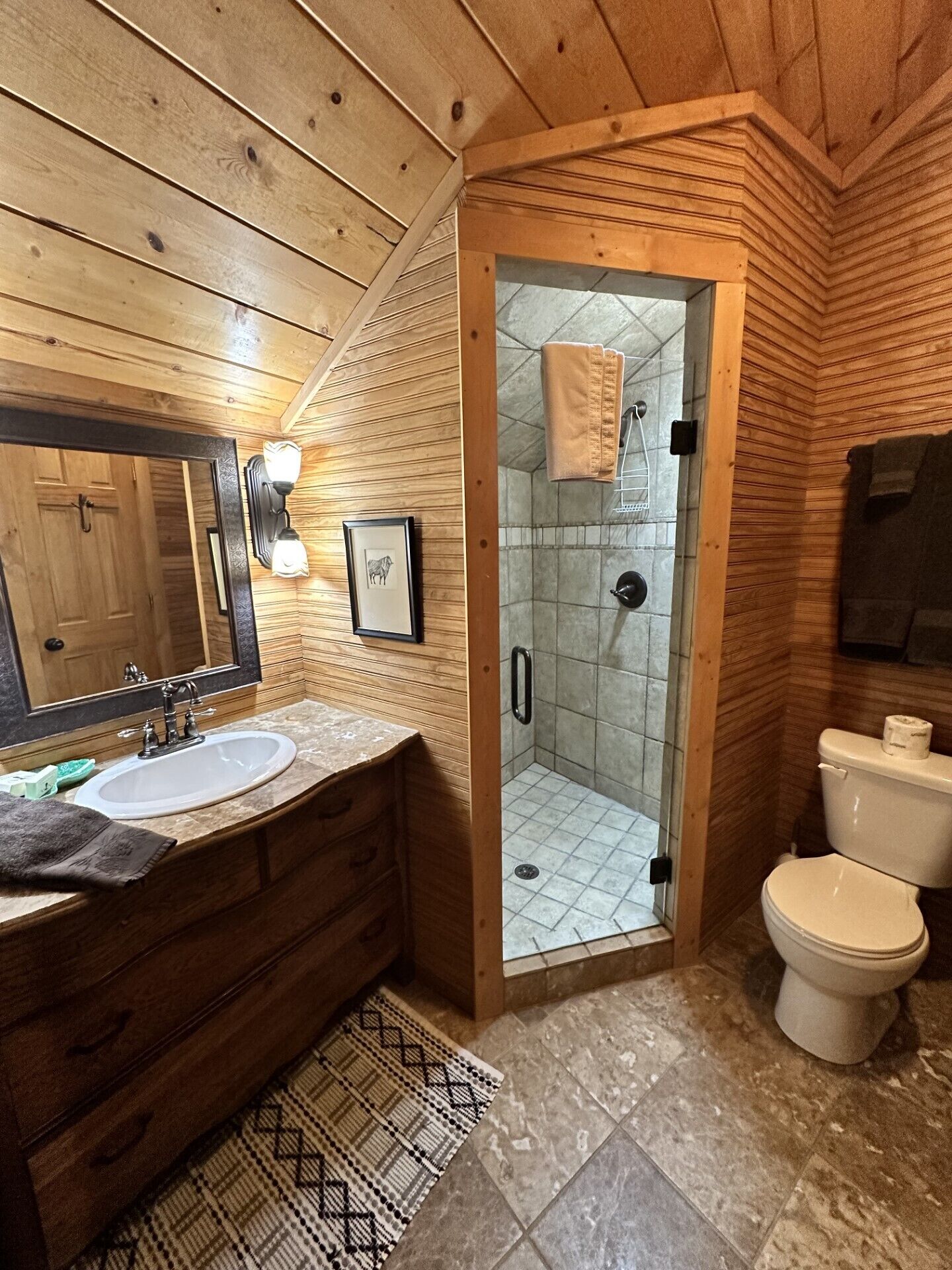 Ein Badezimmer mit Holzwandverkleidung, einem Waschbecken, einem Spiegel und einer Toilette.