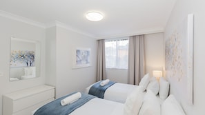 Ein Hotelzimmer mit zwei Betten, einem Schminktisch, einem Spiegel und Bildern an den Wänden.