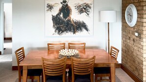 Ein Essbereich mit Holztisch, vier Stühlen, einem dekorativen Mittelstück, einem Bild an der Wand, einer Lampe und einer Uhr.