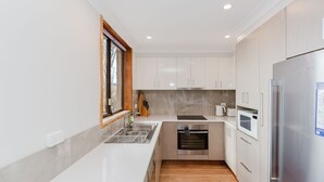 Een moderne keuken met witte kasten, een roestvrijstalen koelkast, een inbouwoven en een raam met uitzicht.