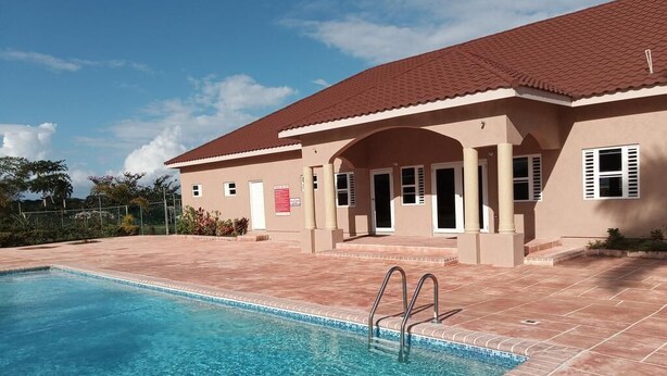 Un bâtiment doté d’une piscine, d’un toit recouvert de tuiles rouges et d’une façade de couleur beige.