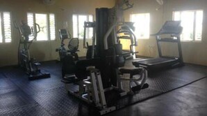 Une salle de sport équipée de matériel d’exercice, d’un tapis de course et de fenêtres avec des stores.