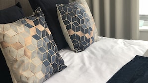 Ein Bett mit weißer Bettwäsche, zwei gemusterten Kissen und einer dunklen Tagesdecke.