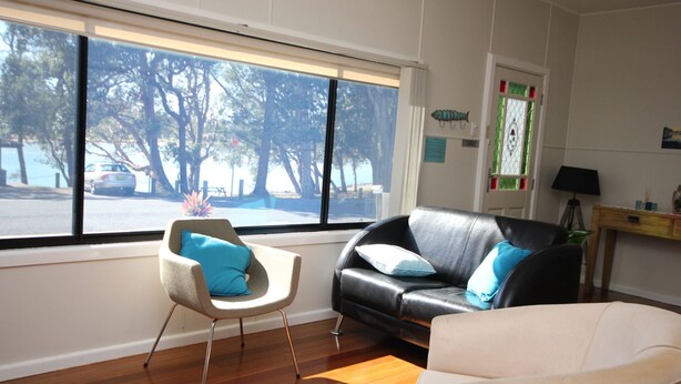 Un salon avec une grande fenêtre, un canapé en cuir noir, un fauteuil blanc et un plancher en bois.