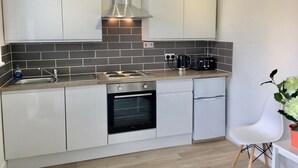 A modern kitchen with white cabinets, a stainless steel range hood, a built-in oven, and a coffee maker on the countertop.