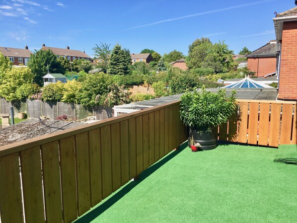 A residential backyard with a wooden fence, green artificial turf, and a potted plant.