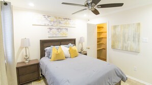 Ein Schlafzimmer mit einem Bett, Nachttischen, einem Deckenventilator und Kunstwerken an den Wänden.