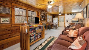 A cozy cabin interior with a wooden ceiling, a bookshelf, a sofa, and a dining area. - ROCKY TOP LOG CABIN-PET FRIENDLY (MAGGIE VALLEY)