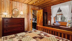 A wooden cabin bedroom with a bed, dresser, and a window with curtains. - ROCKY TOP LOG CABIN-PET FRIENDLY (MAGGIE VALLEY)