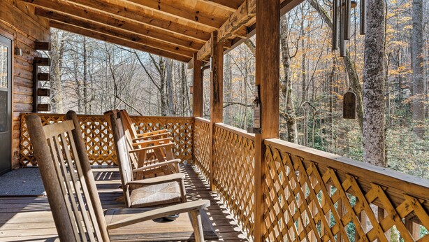 A wooden deck with benches and a lattice railing, overlooking a forested area. - ROCKY TOP LOG CABIN-PET FRIENDLY (MAGGIE VALLEY)