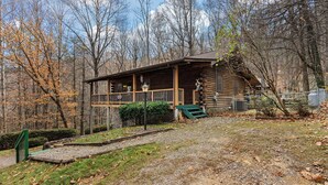 A rustic cabin with a porch, surrounded by trees and a gravel path. - ROCKY TOP LOG CABIN-PET FRIENDLY (MAGGIE VALLEY)